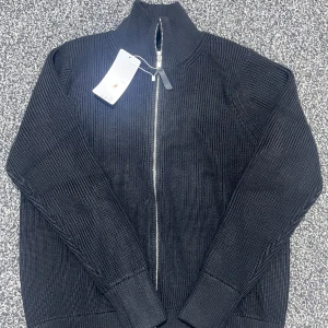 Svart stickad tröja med dragkedja - Säljer en snygg svart stickad tröja från Maison Margiela i storlek S. Tröjan har en dragkedja framtill och är i ett mjukt och bekvämt material. Perfekt för höst och vinter! 🖤