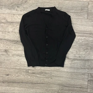 Svart kofta från J.Lindeberg - Säljer en stilren svart kofta från J.Lindeberg i storlek L som passar mer M/S. Den har en klassisk design med knappar framtill. Koftan är i  bra skick och passar utmärkt till höst och vinter, enda defekten visas på bild 4 . Hör gärna av dig vid fler frågor! 😊