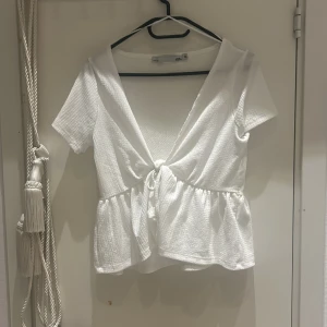 Vit knytblus från Zara - Säljer en superfin vit blus från Zara i storlek S. Den har korta ärmar och en söt knytning framtill som ger en feminin touch. Perfekt för sommardagar eller en avslappnad vårlook. Materialet är lätt och luftigt, vilket gör den bekväm att bära hela dagen.