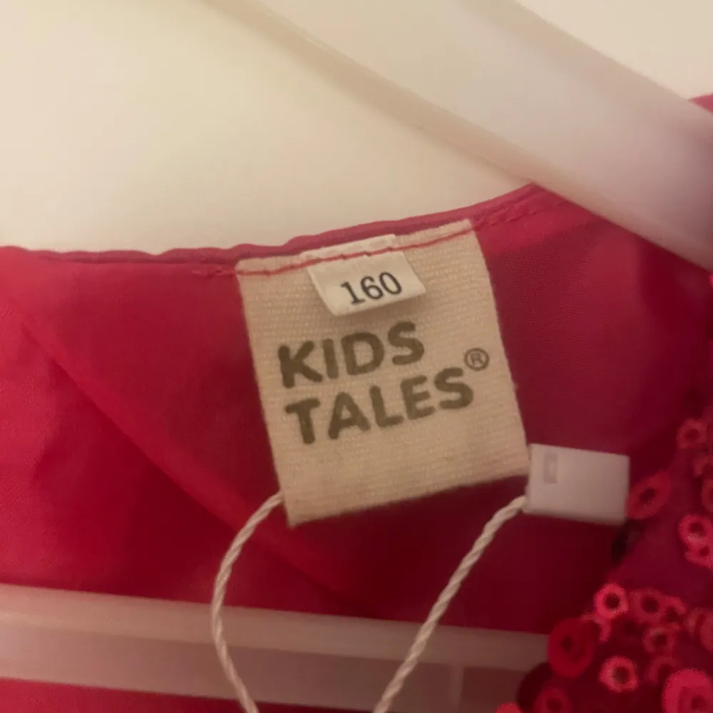 Säljer en superfin röd klänning från Kids Tales i storlek 160. Den har en glittrig paljettöverdel och en fluffig tyllkjol. Perfekt för festliga tillfällen! Klänningen har en söt rosett i midjan och är ärmlös. Ny med taggar kvar!. Klänningar.