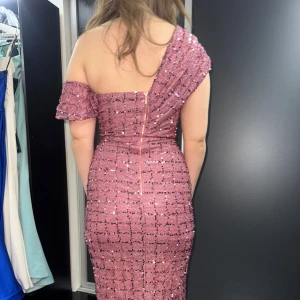 Rosa glittrig klänning - Säljer en superfin rosa glittrig klänning med en axelbandslös design och en smickrande slits framtill. Klänningen har en dragkedja bak och är perfekt för festliga tillfällen. Den är oneshoulder och har en tight passform som framhäver figuren.