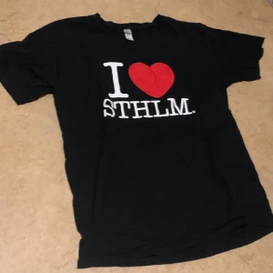 Svart t-shirt med 'I ❤️ STHLM' tryck - Säljer en svart t-shirt med det klassiska 'I ❤️ STHLM' trycket i vitt och rött. Perfekt för alla Stockholm-älskare! T-shirten är kortärmad och i bomull, vilket gör den skön och lätt att bära. Passar bra till vardags eller som en souvenir.PRIS KAN DISKUTERAS 😇😇