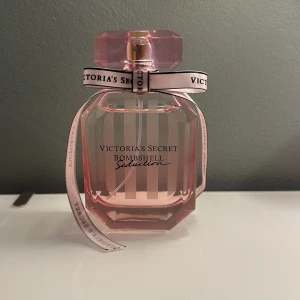 Victoria's Secret Bombshell Seduction Parfym - Säljer en lyxig parfym från Victoria's Secret, Bombshell Seduction. Flaskan är elegant med rosa toner och en söt rosett runt halsen. Perfekt för att känna sig extra glamorös och självsäker. Passar både till vardags och fest!