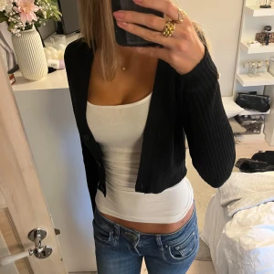Svart ribbad kofta - Säljer en snygg svart ribbad kofta med långa ärmar. Den är croppad och har knappar framtill. Perfekt för både vardag och fest! 🖤🖤