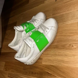 Valentino sneakers med gröna detaljer - Säljer ett par snygga Valentino sneakers i vitt med coola gröna detaljer. Skorna har snörning och är i bra skick, perfekta för både vardag och fest. De är bekväma och stilrena, en riktig statement piece för garderoben!