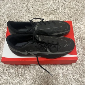 Svarta Nike fotbollsskor - Säljer ett par svarta Nike Phantom fotbollsskor i mycket bra skick. Skorna har en snygg design med silverdetaljer och snörning. Perfekta för fotbollsträning eller match. De har en robust sula med dobbar för bra grepp på planen.