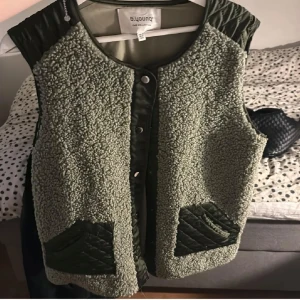 Olivgrön teddyväst  - Säljer en supermysig olivgrön teddyväst från b.young. Västen har coola detaljer och knappar framtill. Perfekt för höst och vinter. Den är knappt använd och i mycket bra skick. Priset kan diskuteras 💕