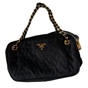Svart quiltad väska från Prada - Säljer en elegant svart quiltad väska från Prada. Den har en snygg kedja i guld och en praktisk dragkedja. Perfekt för både vardag och fest! 🖤