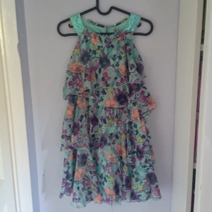 Blommig klänning från Lindex Kids - Säljer en superfin blommig klänning från Lindex Kids i storlek 146/152. Klänningen har ett färgglatt mönster med volanger och är ärmlös. Perfekt för sommarens alla fester! 🌸