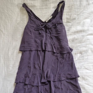 Lila sidenklänning från Feeling - Säljer en superfin syrenlila klänning från Feeling i 100% siden. Den har en vacker volangdesign och knytning fram. Perfekt för sommarens fester eller en mysig vårdag. Klänningen är i storlek L och känns både lyxig och bekväm. Pris är diskuterbart!