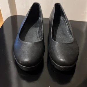 Svarta ballerinaskor  - Säljer ett par svarta ballerinaskor med rund tå och diskret platåsula. Skorna är i syntetmaterial och har en stilren, minimalistisk design som passar till många olika outfits. Storlek 37.