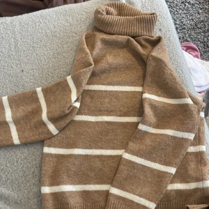 Beige och vit randig polotröja från Lindex - Mysig stickad polotröja från Lindex i beige med vita ränder. Tröjan har lång ärm, ribbade muddar och hög polokrage. Perfekt för kyligare dagar och enkel att matcha med jeans eller kjol.💕