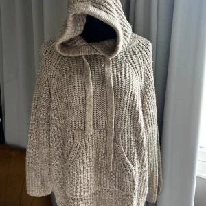 Beige stickad hoodie  - SÅ SNYGG mysig beige stickad hoodie med stor känguruficka framtill och huva. Tröjan har en avslappnad passform och är perfekt för kyliga dagar. Grovstickat material ger en trendig och avslappnad look. 