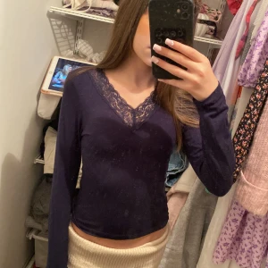 Mörkblå långärmad topp med spets - Säljer en mörkblå långärmad topp med v-ringning och dekorativ spets runt halsen. Toppen är figurnära och passar perfekt till många olika outfits. Materialet känns mjukt och stretchigt.