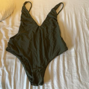 Olivgrön baddräkt med djup v-ringning - 40kr Storlek S-M En stilren olivgrön baddräkt med smala axelband och djup v-ringning både fram och bak. Modellen har hög benskärning och är enkel utan mönster eller extra detaljer. Perfekt för strand eller pool.