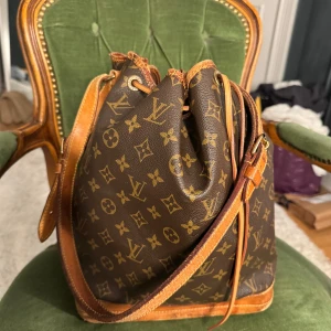 Louis Vuitton Monogram Noé axelväska - Säljer en klassisk brun axelväska från Louis Vuitton i monogram canvas med detaljer i ljust skinn. Väskan är köpt på Veistaire för ca 7500kr💗Kan mötas upp i Sthlm!