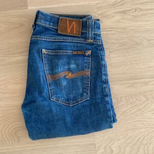Blå jeans från Nudie Jeans - Säljer ett par klassiska blå jeans från Nudie Jeans med raka ben och snygga kontrastsömmar. Byxorna har fem fickor och normal passform. Perfekta för dig som gillar stilrena och tidlösa jeans.