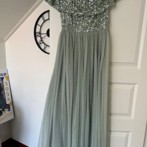 Ljusgrön långklänning med paljetter - Säljer en elegant ljusgrön långklänning med glittrig paljettöverdel och mjukt, fallande kjol i tyll. Klänningen har korta ärmar och en vacker, romantisk känsla – perfekt för bal eller fest.