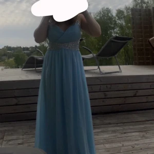 Ljusblå långklänning med pärldetaljer - Säljer en elegant ljusblå långklänning med v-ringad omlott-topp och pärlbroderier i midjan och runt halsringningen. Som jag köpte på Plick. Använd 1-2 ggr och fint skick, inget fast pris💕 hör av vid fler frågor 