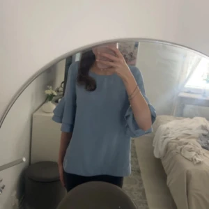 Ljusblå blus med volangärmar - Säljer en ljusblå blus med rund halsringning och snygga volangärmar. Blusen har en lös passform och är tillverkad i ett mjukt, lätt material som känns skönt mot huden. Perfekt till sommaren 🫐