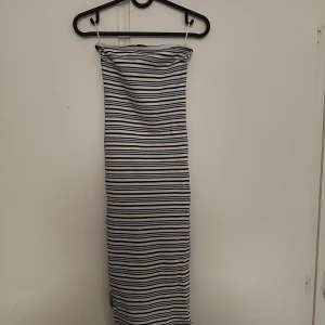 Randig axelbandslös klänning - Säljer en axelbandslös långklänning med smala blå och vita ränder. Klänningen har en tight passform och är perfekt för sommardagar. Mjuk och stretchig känsla, enkel att styla med sneakers eller sandaler.