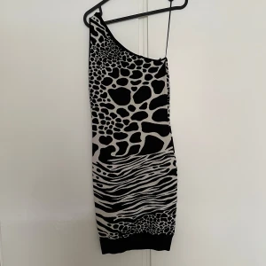 Svart och vit one shoulder klänning från Michael Kors - Säljer en snygg one shoulder klänning från Michael Kors i svart och vit med zebramönster. Klänningen är tight och har en unik asymmetrisk axel. Perfekt för dig som vill sticka ut!