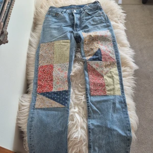 Levis 501 jeans med patchwork - Unika Levis 501 jeans med patchwork i olika färger och mönster på framsidan av benen. Klassisk ljusblå denim med raka ben och hög midja. Perfekt för dig som vill sticka ut med en kreativ och personlig stil.