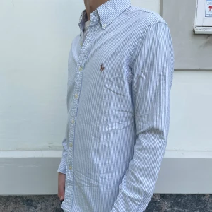 Polo Ralph Lauren skjorta - Säljer en klassisk ljusblå och vit randig skjorta från Ralph Lauren. Skjortan har lång ärm, knappar framtill och broderad logga på bröstet. Slim fit-modell som passar perfekt till många tillfällen. Nypris är 2149. Hör av er vid några frågor. 