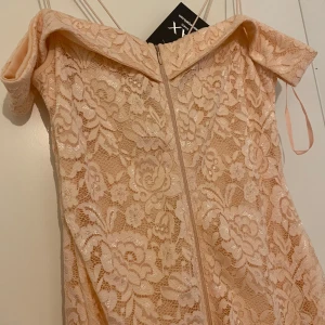 Ljusrosa spetsklänning från AX Paris - Säljer en ljusrosa axelbandslös spetsklänning från AX Paris med vacker blommig spets och offshoulder-detalj. Klänningen har smala axelband och dragkedja bak. Perfekt för speciella tillfällen!
