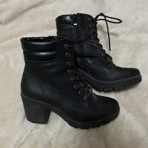 Svarta boots med klack och snörning - Säljer ett par svarta boots med grov klack och snörning framtill. Skorna har dragkedja på sidan för enkel påtagning och en rund tå. Perfekta för att lyfta din outfit med en tuff touch.