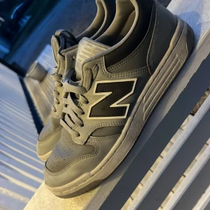 Grå New Balance sneakers - Säljer ett par grå New Balance sneakers med vit sula och svart/vit N-logga på sidan. Skorna har snörning och rund tå, samt perforerade detaljer framtill för extra ventilation. Perfekta för en sportig och stilren look.