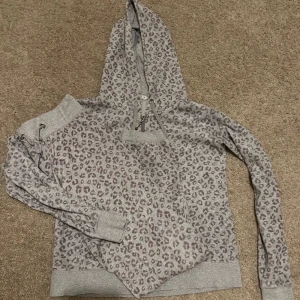 Grå leopardmönstrad mjukis set  - Säljer en grå mjukis set med leopardmönster och huva. Tröjan har långa ärmar, ribbade muddar och en stor ficka framtill. Perfekt för en avslappnad stil och mysiga dagar. Priset kan diskuteras vid snabb affär 