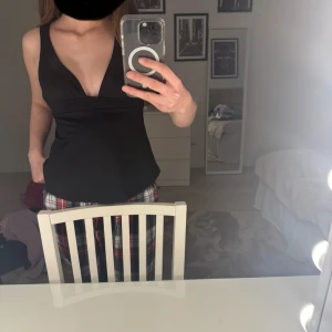 Svart v-ringad linnetopp med knyt i ryggen - Säljer en svart v-ringad linnetopp med breda axelband och knytning i ryggen. Toppen har en figurnära passform och är perfekt för varma dagar eller som ett lagerplagg.