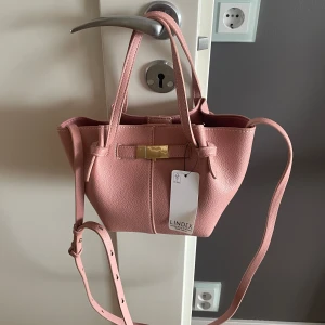 Rosa axelväska från Lindex - Stilren rosa axelväska från Lindex med justerbar axelrem och två handtag. Perfekt liten väska till sommaren. Väskan är helt oanvänd, prislapp finns kvar!💕
