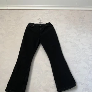 Svarta bootcut jeans från ASOS  - Svarta jeans från ASOS DESIGN med bootcut passform. Klassisk femficksmodell med knapp och dragkedja framtill. Jeansen är tillverkade i ett mjukt denimtyg och har en stilren look som passar till många olika outfits.