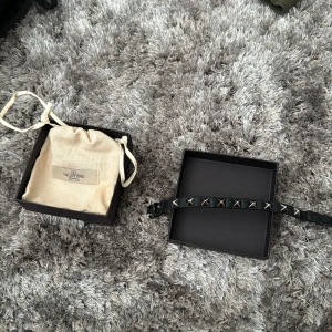 Valentino armband  - Säljer ett svart Valentino armband  med silverfärgade pyramidformade nitar. Armbandet är smalt och har en klassisk spänne. Perfekt accessoar för att ge din outfit en edgy touch.