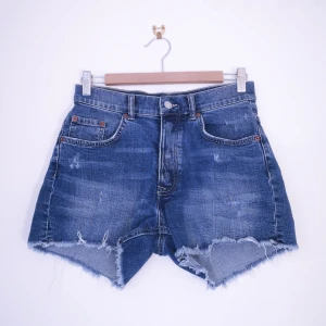 Jeansshorts - Lindex Vintage strl 38 - Distressed jeansshorts från Lindex Vintage. Hög midja, lite stretch, två fickor fram, två bak. Öppnas med knappar. Mått - 75cm i midjan. Kan ta fler bilder och mått vid intresse. 