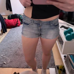Ljusblå jeansshorts lågmidjade  - Säljer ett par ljusblå jeansshorts med fransig kant nertill och klassiska fem fickor. Shortsen har låg midja och en normal passform. Perfekta för varma dagar!