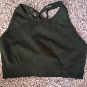 Svart ribbad linnetopp med korsade band define iciw - Snygg svart ribbad linnetopp med högt skuren hals och korsade band i ryggen. Perfekt för träning eller chill dagar. Toppens material är stretchigt och sitter tight mot kroppen för en sportig look.