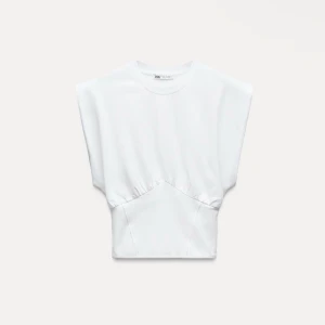 Vit croppad topp från Zara - Säljer en vit croppad topp från Zara med breda axlar och markerad midja. Toppen har en cool metallspänne bak och är tillverkad i mjuk bomull. Perfekt för dig som gillar minimalistisk och trendig stil.