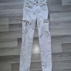 Vita cargobyxor från UNIQ MINI, stl 152 - Snygga vita cargobyxor från UNIQ MINI i storlek 152. Byxorna har flera fickor, bland annat med dragkedja på benen, och klassisk cargostil. De är tillverkade i ett mjukt bomullsmaterial och har normal passform med raka ben. De har några ljus gula fläckar vid gylfen. Vet inte om de går att få bort, har inte försökt.