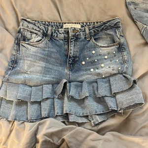 Jeanskjol med volanger och pärlor - Superfin jeanskjol från Zara med volanger nertill och pärldetaljer på ena fickan. Perfekt för dig som vill sticka ut lite extra!