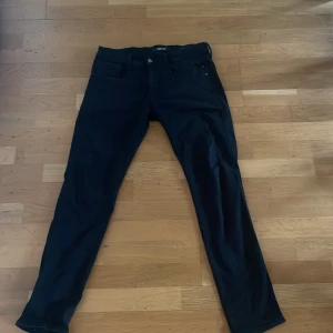 Svarta Replay Hyperflex jeans - Säljer ett par svarta Replay Hyperflex jeans i modellen anbass med klassisk femficksdesign och smal passform. Jeansen är tillverkade i stretchigt material för extra komfort. Storleken är 31/32. Perfekta för dig som gillar stilrena och bekväma jeans. Jeansen är välanvända utan några större slitage därav det låga priset då nypris ligger runt 1500. Priset är inte hugget i sten och jag är villig att förhandla/ kan erbjuda ett bättre pris om man skulle köpa någonting mer från mig som ett paket pris