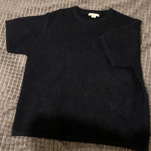 Svart stickad tröja Gina Tricot - En svart stickad tröja från Gina Tricot med korta ärmar och rund halsringning. Tröjan har en enkel och clean look, perfekt att styla med jeans eller kjol. Mjuk och skön känsla tack vare det stickade materialet. Storlek 170 barn 