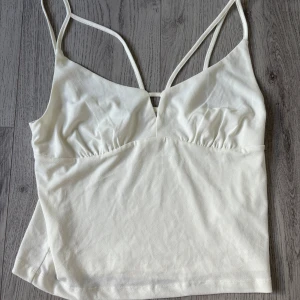 Vit linnetopp från BikBok - Säljer en stilren vit linnetopp från BikBok med tunna axelband och lätt v-ringning framtill. Toppen har en enkel och fräsch design med lätt rynkade detaljer under bysten. Perfekt att matcha med jeans eller kjol för en clean look. Helt oanvänd 