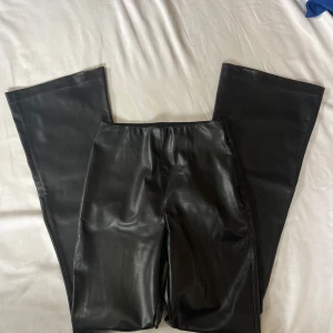 Svarta bootcut byxor i skinnimitation H&M - Snygga svarta bootcut byxor från H&M i skinnimitation. De har hög midja och vida ben. Slitna längst ner (se bild)