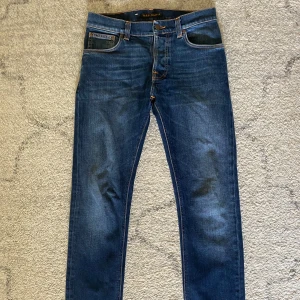 Blå jeans från Nudie Jeans Co - Snygga blå jeans från Nudie Jeans Co med klassisk femficksdesign och kontrastsömmar. Jeansen har en rak passform och är tillverkade i slitstarkt bomullsjeans. Perfekta för dig som gillar en tidlös och stilren look. Storlek 27/32