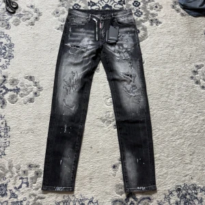 Svarta skinny jeans från Dsquared2 - Riktigt snygga svarta skinny jeans från Dsquared2 med slitningar, blekta detaljer och coola färgstänk. Jeansen har dragkedja framtill och klassisk femficksdesign. Perfekta för dig som vill sticka ut med en edgy streetstil. Stl 32 motsvarar 48 