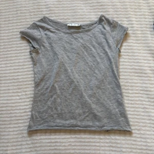 Grå t-shirt från Lager 157 Angelology XS - Enkel och stilren grå t-shirt från Lager 157 Angelology i storlek XS. T-shirten har rund halsringning, korta ärmar och en liten broderad vingdetalj i nacken. Perfekt basplagg i mjuk bomullskänsla.