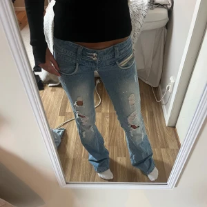 Blå slitna bootcut jeans Olala - Säljer nu mina absoluta favorit jeans med låg midja jag har sytt ner dom för att få dom mer lågmidjade, grenhöjden: 15 cm innebenslängden:83cm midjemåttet: 40 cm. Jeansen har slitna detaljer, små glittriga stenar och dragkedja på fickan. Snygga kristallknappar framtill, skriv om ni har frågor!💓och skriv även gärna innan ni köper!